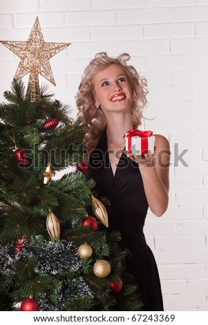 The beautiful girl with a gift stands near a Christmas tree.