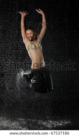 The beautiful girl dancing in water under rain on a black background.  Modern dances.