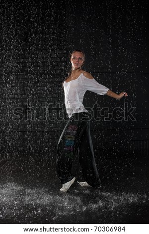 The beautiful girl dancing in water under rain on a black background.  Modern dances.