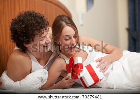 Happy young family with gift box lies in the bed at home. Valentine\'s Day