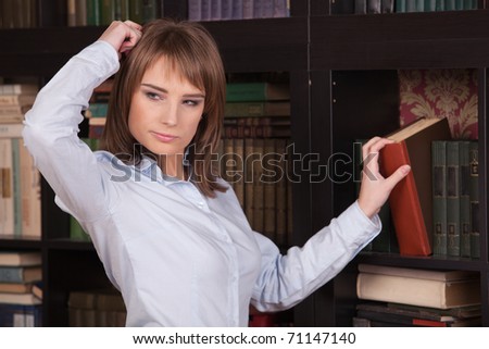 Clever young woman stands in front of  bookshelves and chooses the book.