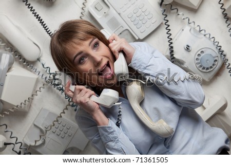Stressed  young businesswoman with telephones in her hands.