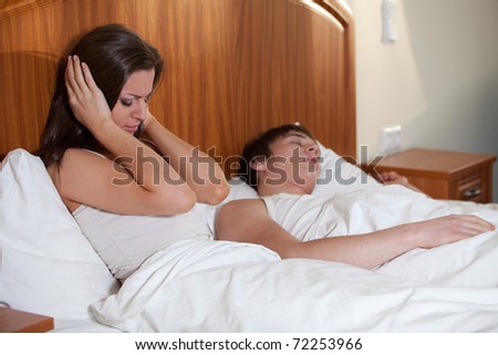Unhappy woman and her snoring husband in bedroom.