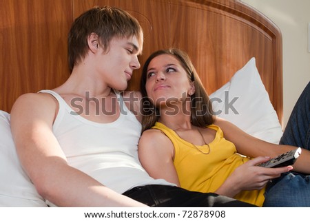 Happy young couple  lies in the bed at home and watches TV.