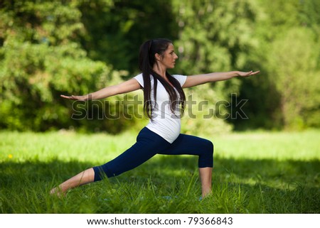 The active pregnant woman does sports exercises in a summer park. Care of health and pregnancy.