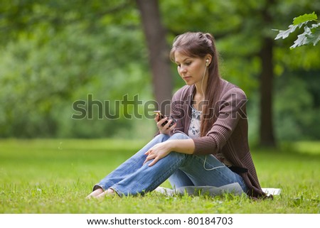 Young beautiful woman with earphones sits on the green grass  in the park.