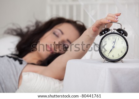Young sleeping woman and alarm clock in bedroom at home.