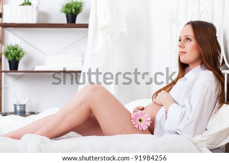 Pregnant woman with flower lies on the house bed.
