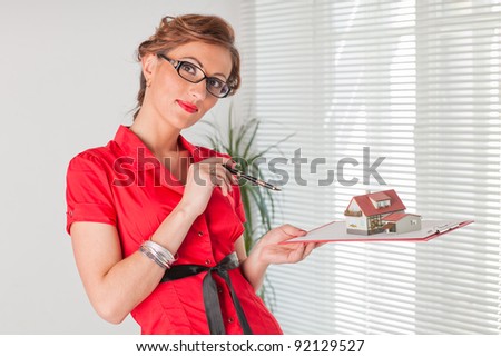Young businesswoman showing a model of house stands at the office. House purchase concept.