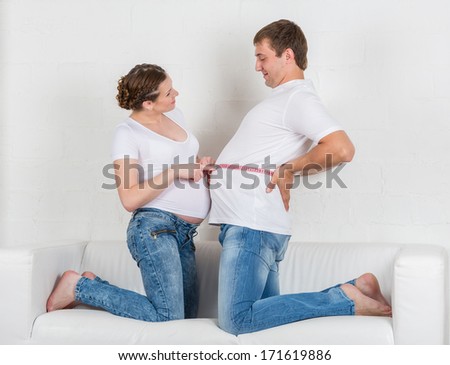 Happy pregnant family with measuring tape sit on the sofa in the room.