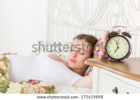 Young sleeping  pregnant woman and alarm clock in the bedroom.  Selective focus on a alarm clock.