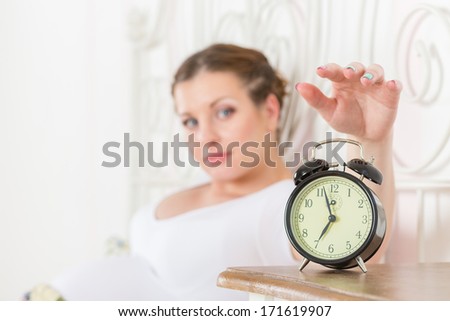 Young sleeping  pregnant woman and alarm clock in the bedroom.  Selective focus on a alarm clock.