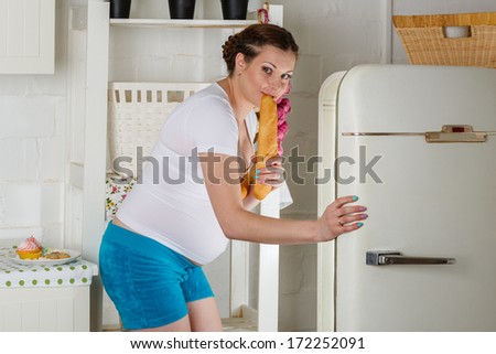 Hungry young pregnant woman stands near refrigerator and searches the food.