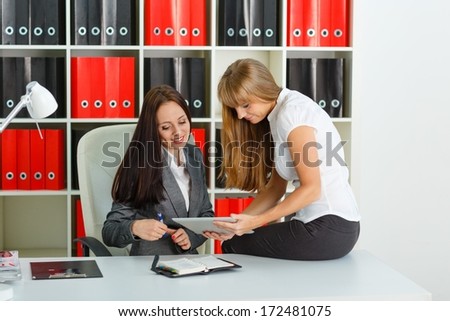 Two young business women  with computer tablet and daily log sit in the office.