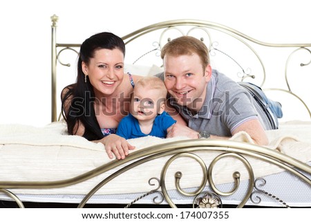 Young parents with their sweet child lie on the bed on a white background. Happy family.