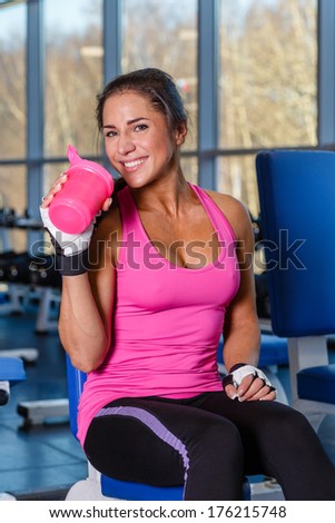The sports young woman with a protein cocktail in a shaker sits in a gym. Sports nutrition.
