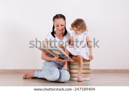 Young mother and little daughter read the books in the room. Happy family. Early development and learning.
