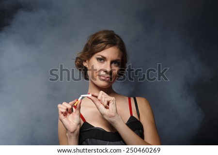 Happy young confident woman, quitting smoking, stands with the broken cigarette on a dark background with smoke. Concept - fight against smoking.