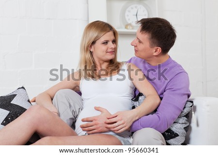 The happy pregnant woman with the husband sitting on a sofa of the house.