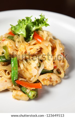 A picture of thai noodle with chicken and vegetables served on a white plate