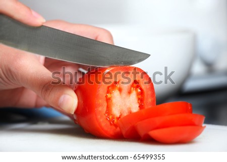 A close-up of a female hand cutting a tomato in the kitchen