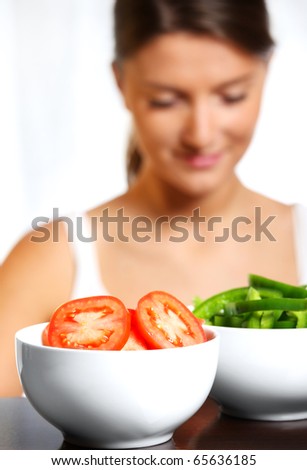 A picture of two white bowls of vegetables with a young wife in the background