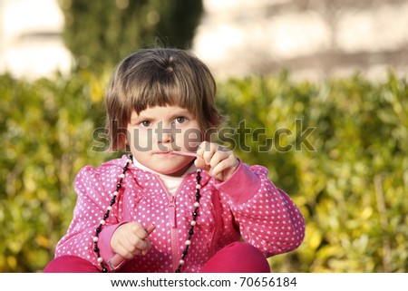 A picture of a little girl sitting in the park and trying to use a lip gloss