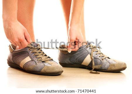 A close-up of a person lacing up too big shoes over white background