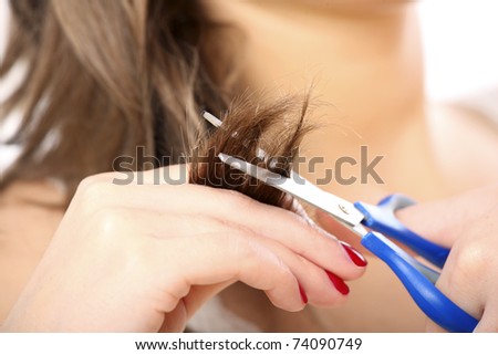 A close up of a woman cutting her hair with blue scissors