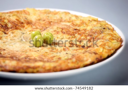 A picture of a typical Spanish tortilla decorated with olives over light background