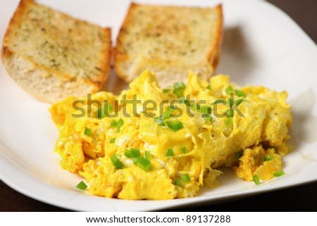 A picture of scrambled eggs with toasted baguette served on a white plate