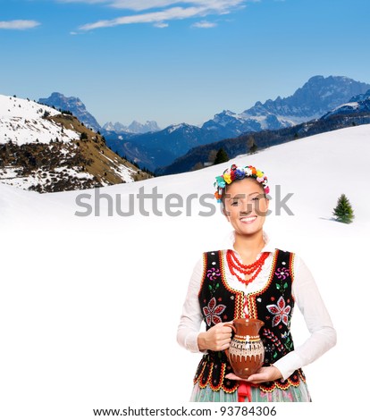 A portrait of a beautiful and hospitable Polish woman in a traditional outfit over mountains in winter