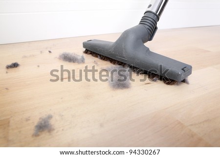 A picture of a vacuum cleaning wooden floor covered with dust