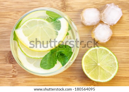 A picture of a glass of water with lemon lime and mint served with ice cubes on a wooden board