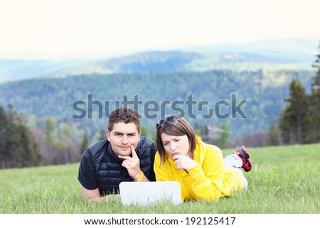 A picture of a young couple and laptop on the grass in the mountains