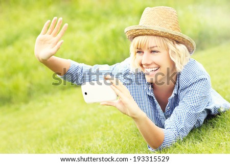 A picture of a woman lying on grass and taking pictures with cellphone