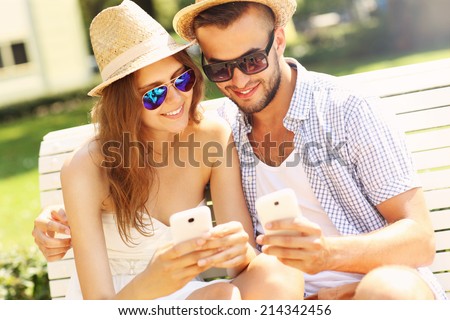 A picture of a young couple sitting on a bench with smartphones