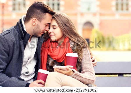 A blurry portrait of a young couple on a bench with smartphone in the park