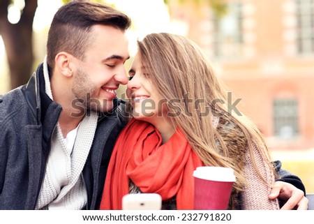 A picture of a young romantic couple kissing on a bench with smartphone in the park