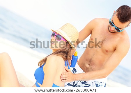 A picture of a man applying sunscreen on the back of his woman at the beach
