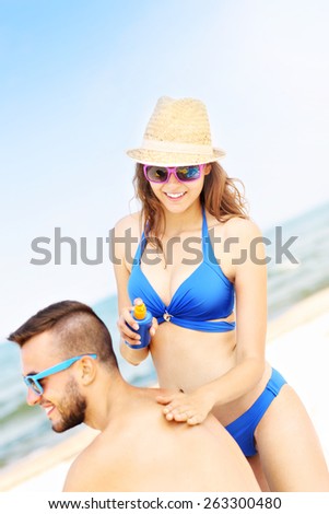 A picture of a woman applying sunscreen on the back of her man at the beach