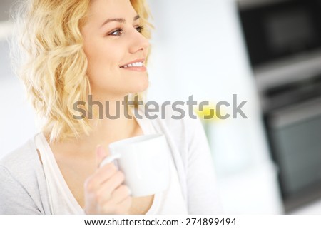 A picture of a young happy woman drinking coffee in the kitchen