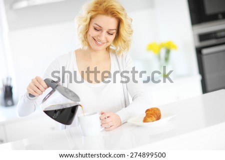 A picture of a young happy woman pouring coffee to a white mug in the kitchen