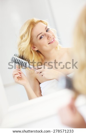 A picture of a happy woman brushing her hair in the bathroom