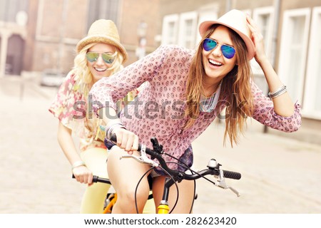 A picture of two girl friends riding a tandem bicycle in the city