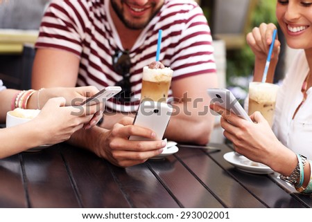 A picture of a group of friends resting in an outdoor cafe and using smartphones