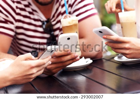 A picture of a group of friends resting in an outdoor cafe and using smartphones