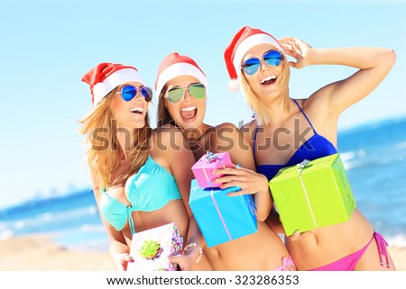 A picture of a group of women in bikini and Santa\'s hats holding presents on the beach