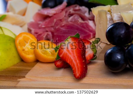 plate of fresh tasty and delicious fruits grape strawberry apple and cheese with jerky on background