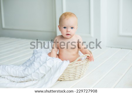 adorable baby girl with fun emotions sitting in basket with blanket at white interior